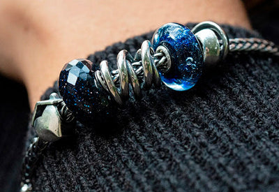 Trollbeads armbånd med Hjem, Søskende og Grib chancen sølvkugler samt to blå glaskugler på et rævehale armbånd