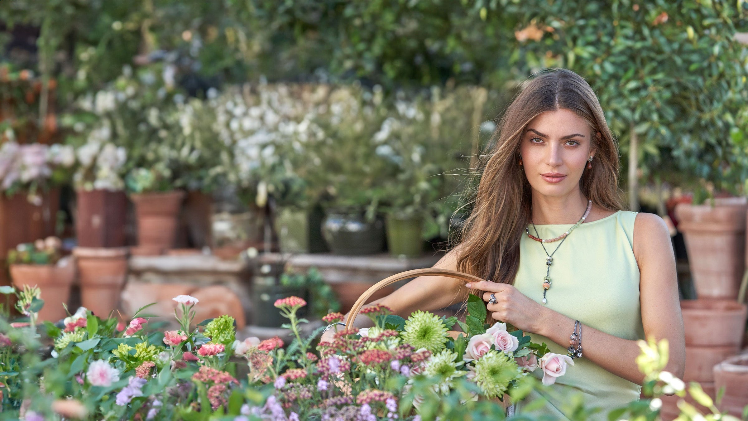Model står i en have med en kurv fuld af blomster iført Trollbeads smykker